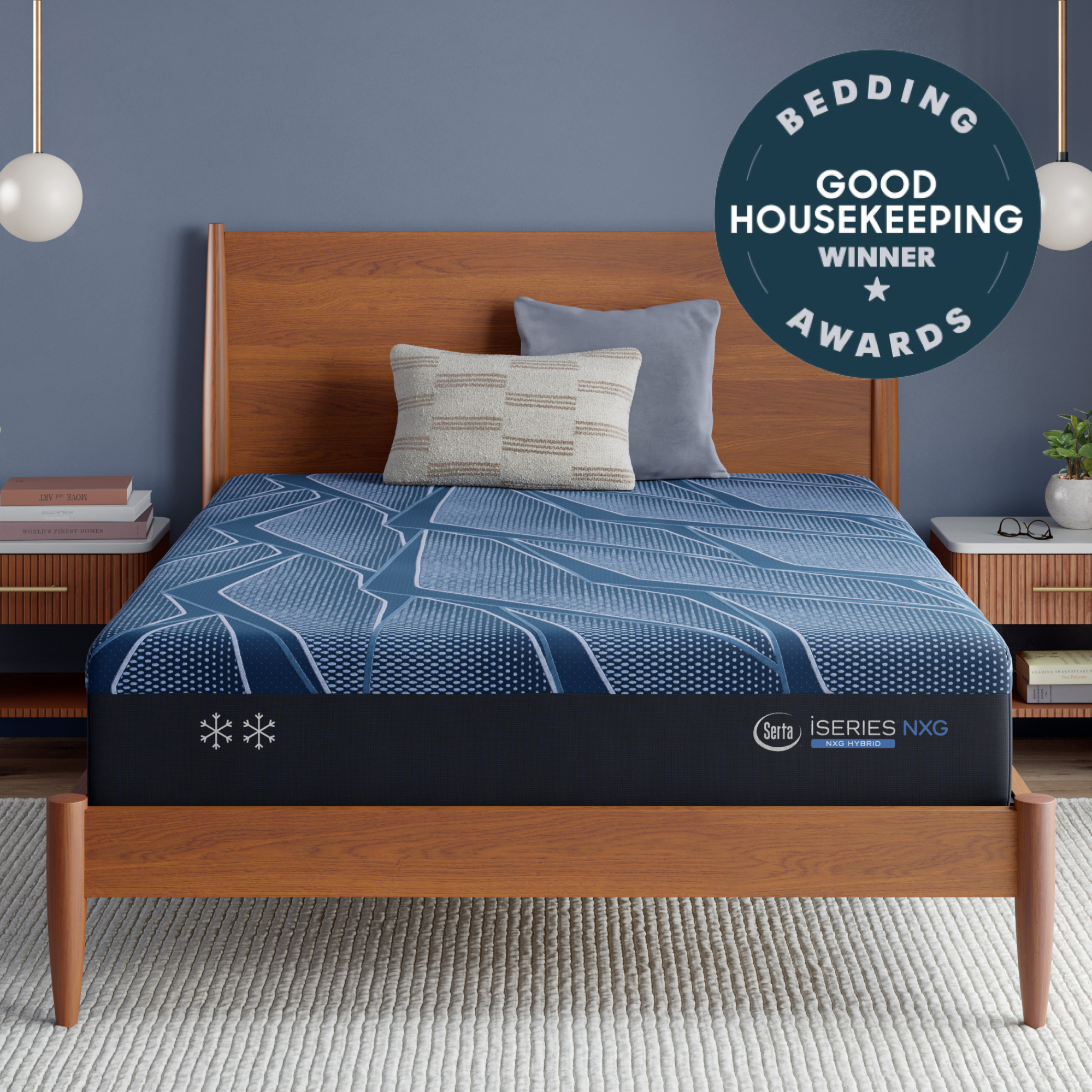 A Blue Serta® iSeries® NXG™ Mattress on a wooden bed frame in a styled bedroom setting, featuring a blue patterned bedding cover, two pillows, a blue wall, and a 'Bedding Good Housekeeping Winner Awards' badge overlay.