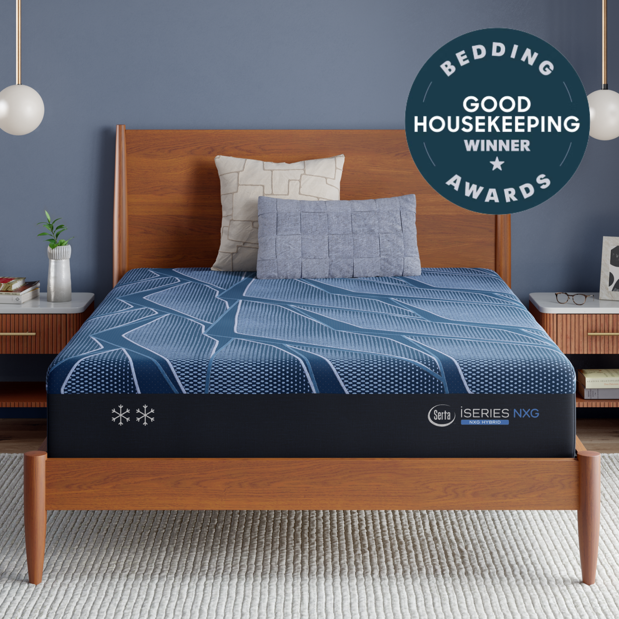A Blue Serta® iSeries® NXG™ Mattress with a blue patterned mattress and matching pillows in a modern bedroom setting with a wooden bed frame, blue-gray walls, and a circular 'Bedding Good Housekeeping Winner Awards' badge in the top right.
