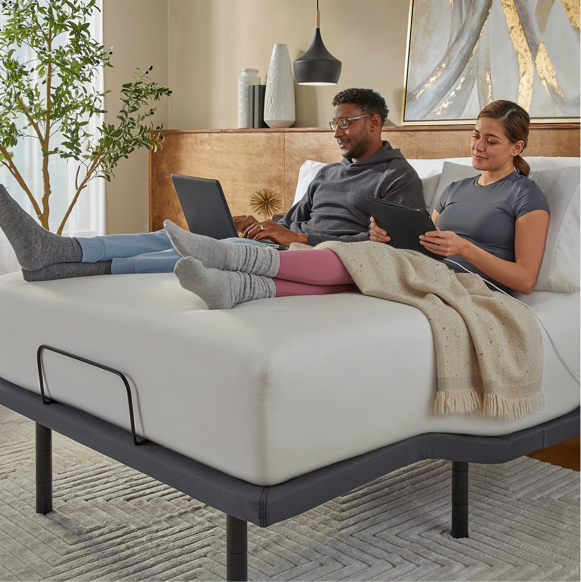 Man and Woman sitting in a Baselogic Gold Adjustable Base with a white mattress on top of it.