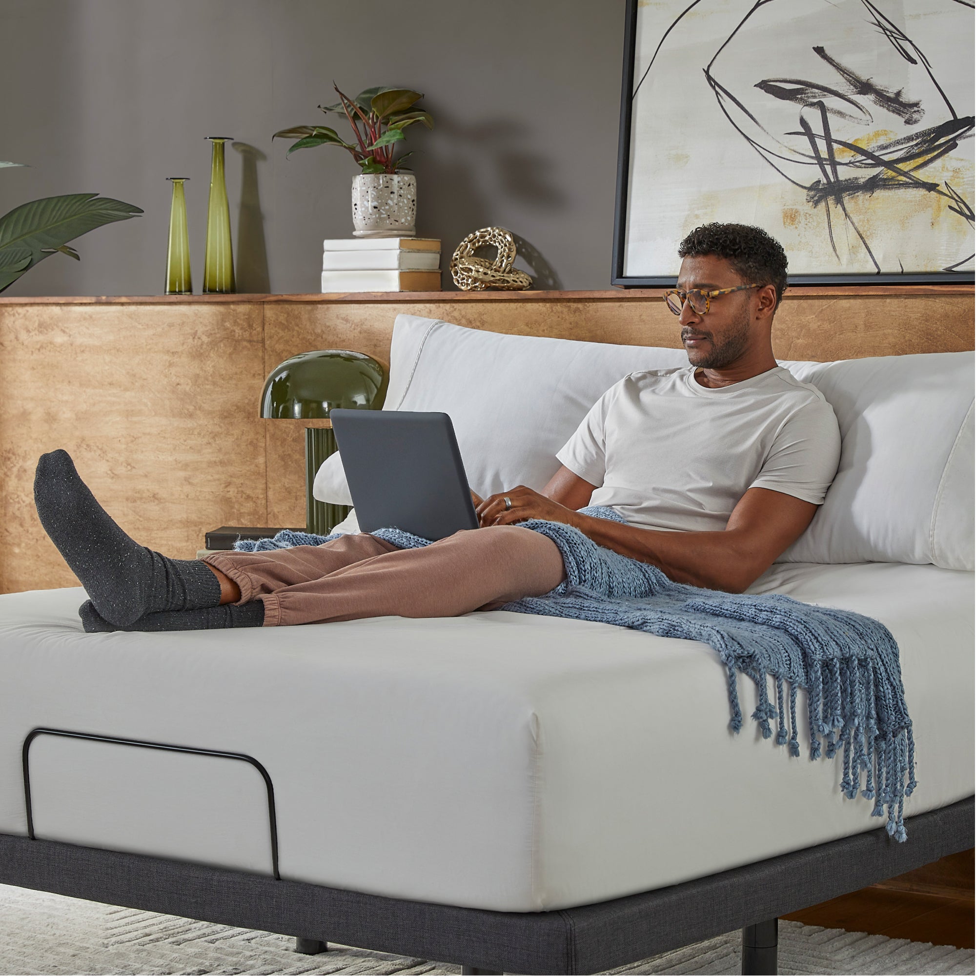 Man with a laptop is sitting on top of a mattress on a baselogic adjustable base
