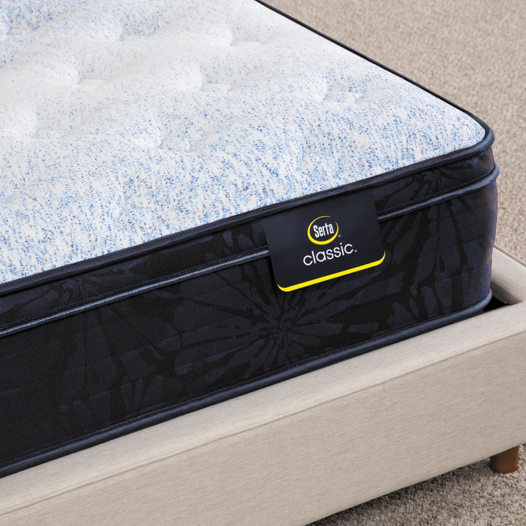 Corner of Serta classic dorian plush euro top mattress sitting in a beige bed frame ||feel: plush euro top ||level: standard
